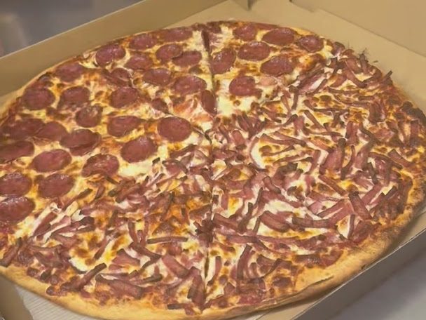 Half pepperoni, half bacon pizza in an open takeaway box