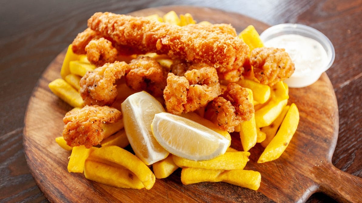 Battered seafood and chips on a timber board with lemon