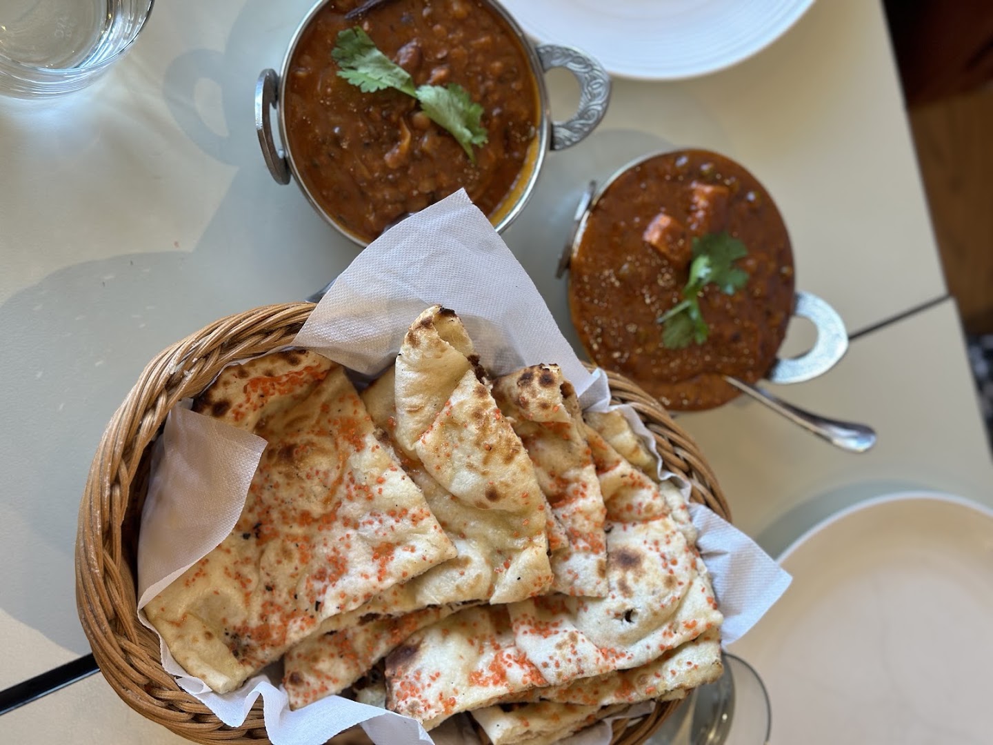 Basket of fresh naan beside copper bowls of dal and curry